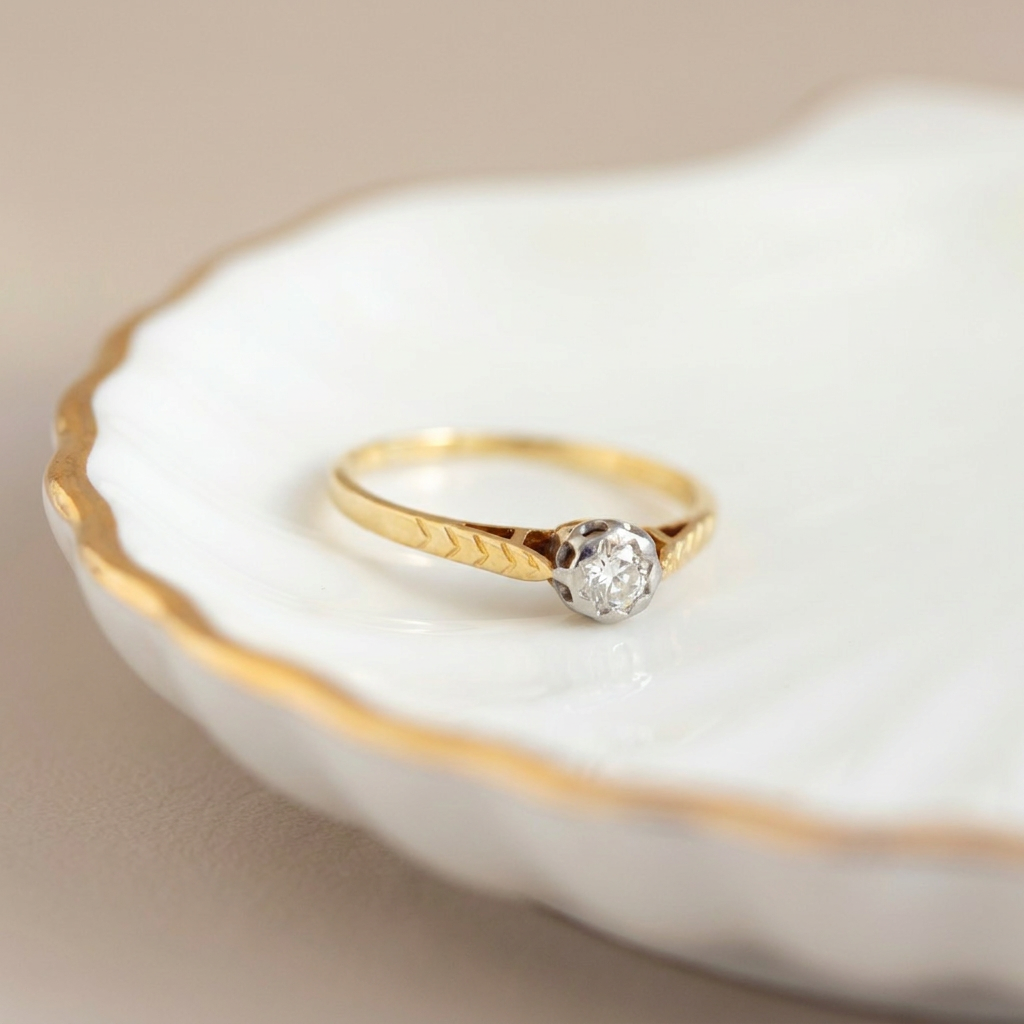 1930s style 18k yellow gold solitaire diamond ring with openwork shoulders on ceramic dish