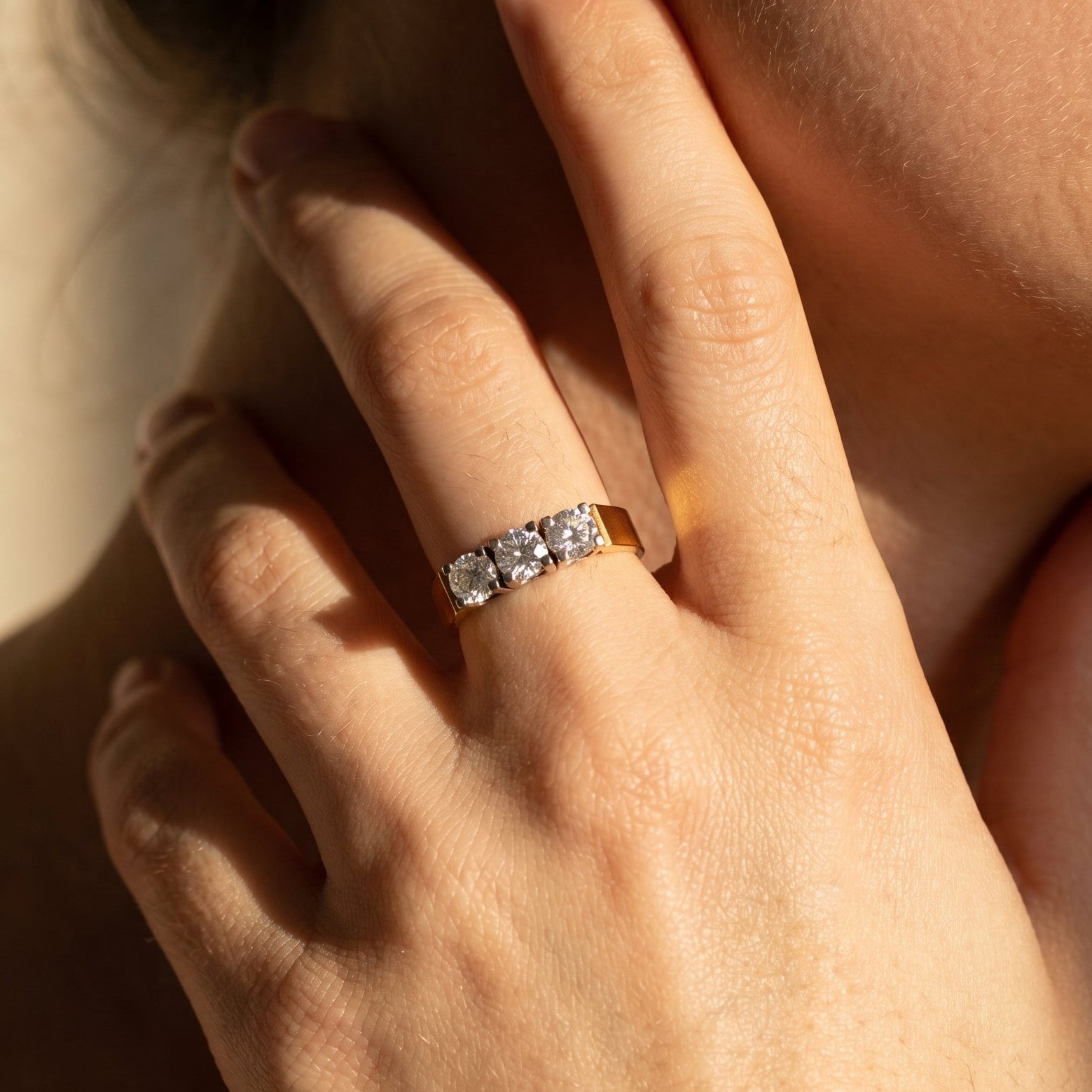 Three-stone diamond ring on hand showing fit and two-tone gold contrast