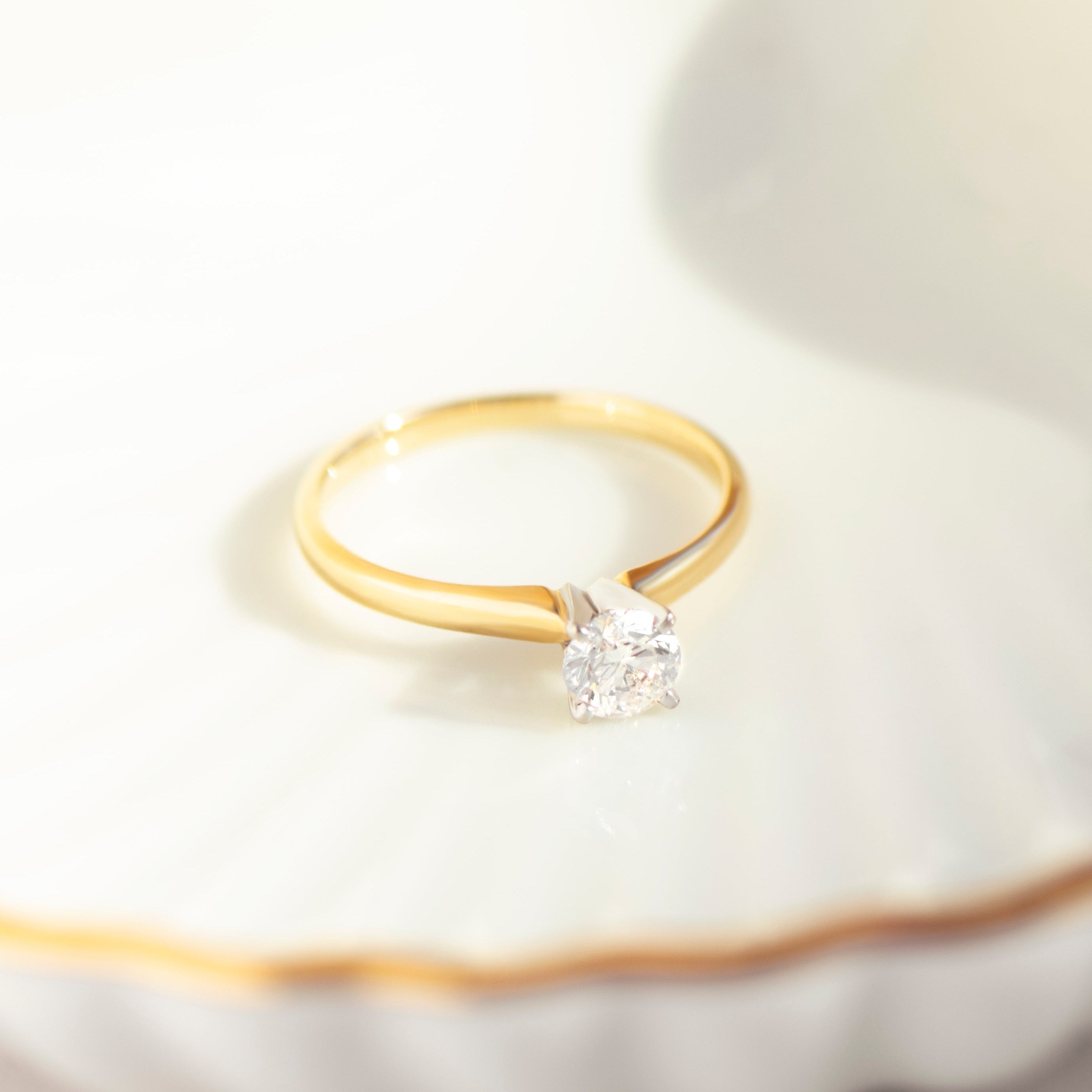 Symmetrical 14k yellow gold solitaire diamond ring on ceramic dish