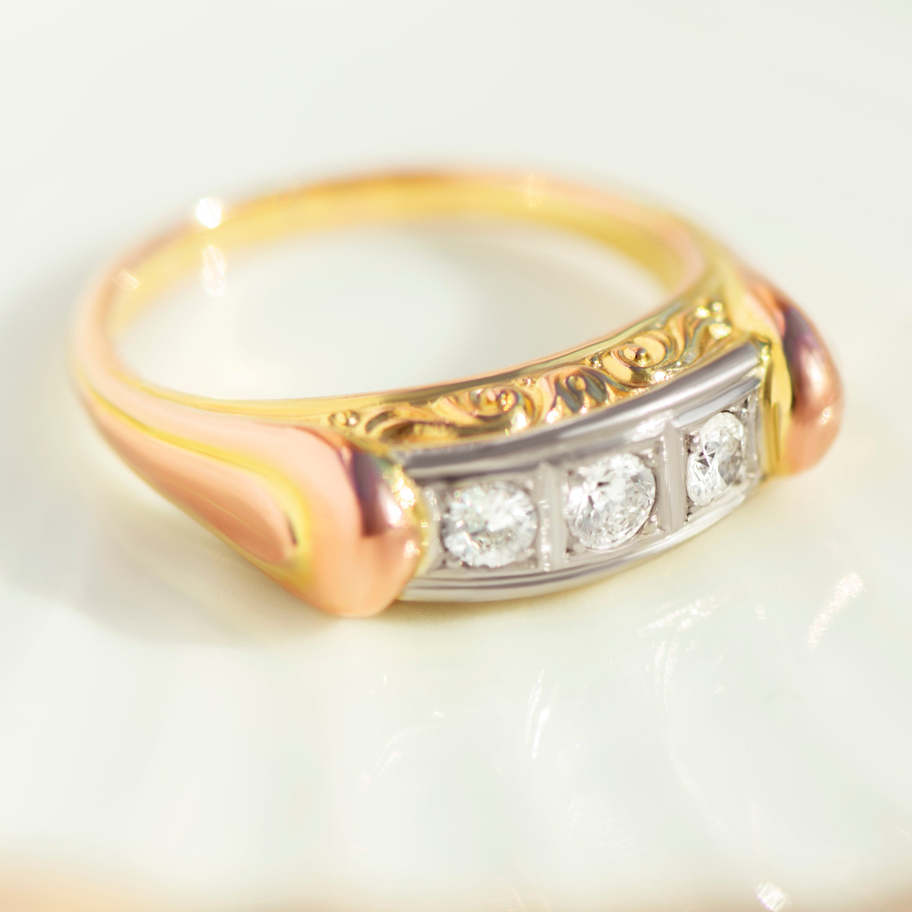 Front view of vintage three-stone diamond ring with white gold setting and decorative engraved yellow red gold band