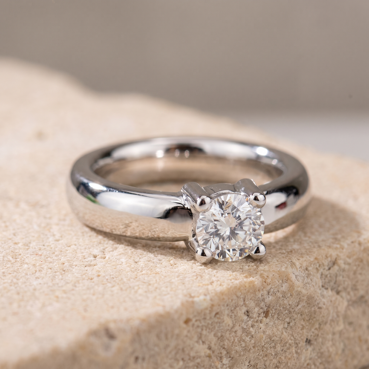 Front view of 18k white gold solitaire diamond ring on textured stone surface